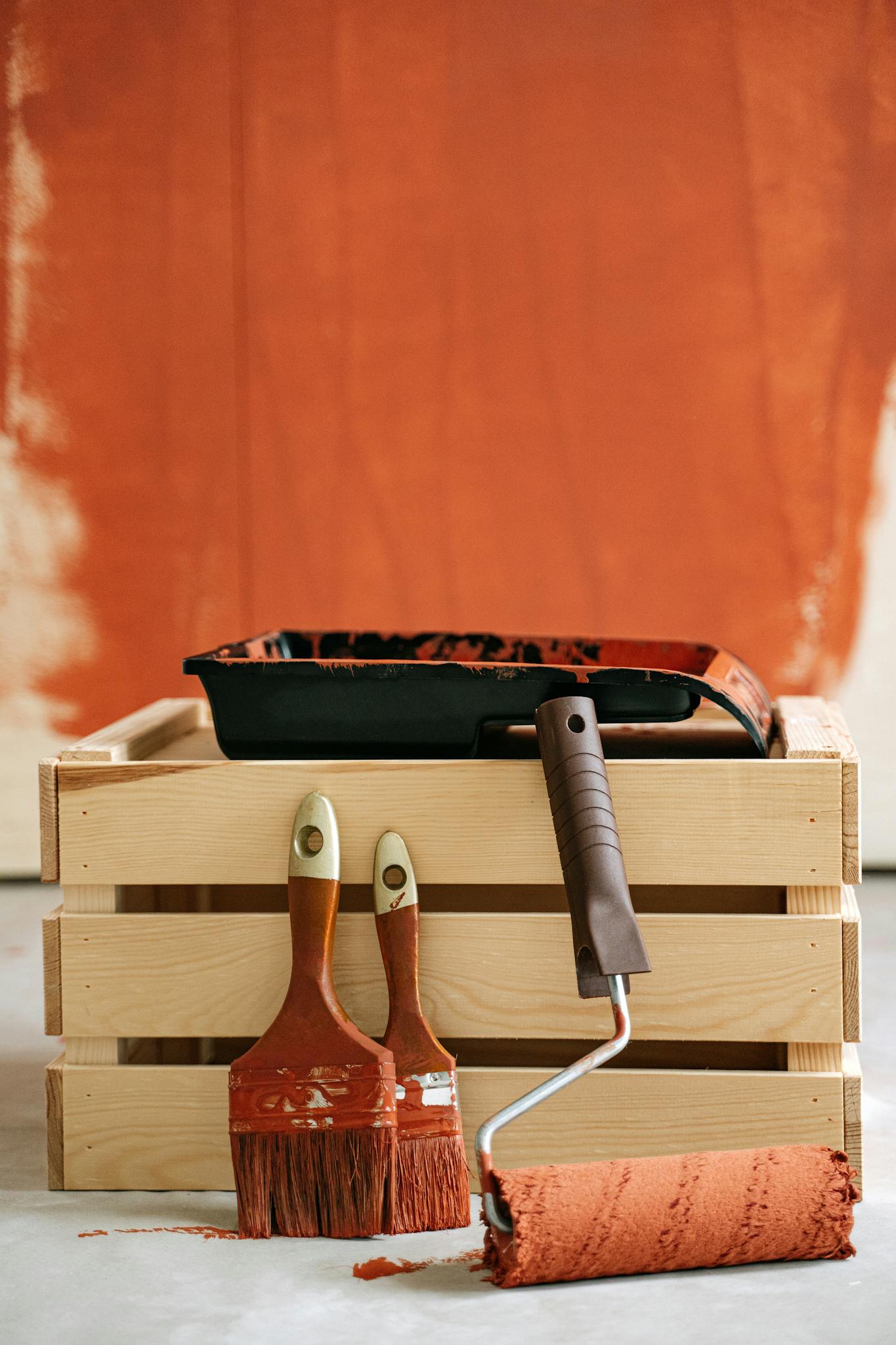 Wooden crate with paintbrushes and roller against a partially painted wall.